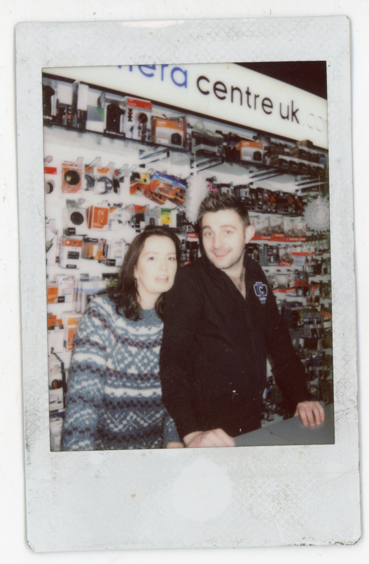 Instax photo of two people under the Camera Centre UK sign inside the shop