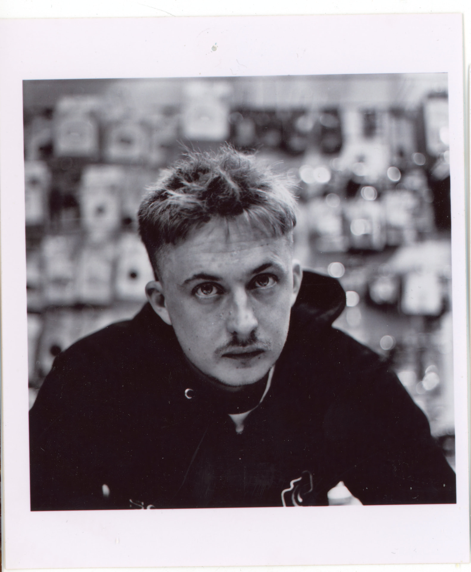 Black and white polaroid portrait of Ieuan behind the counter at Camera Centre UK
