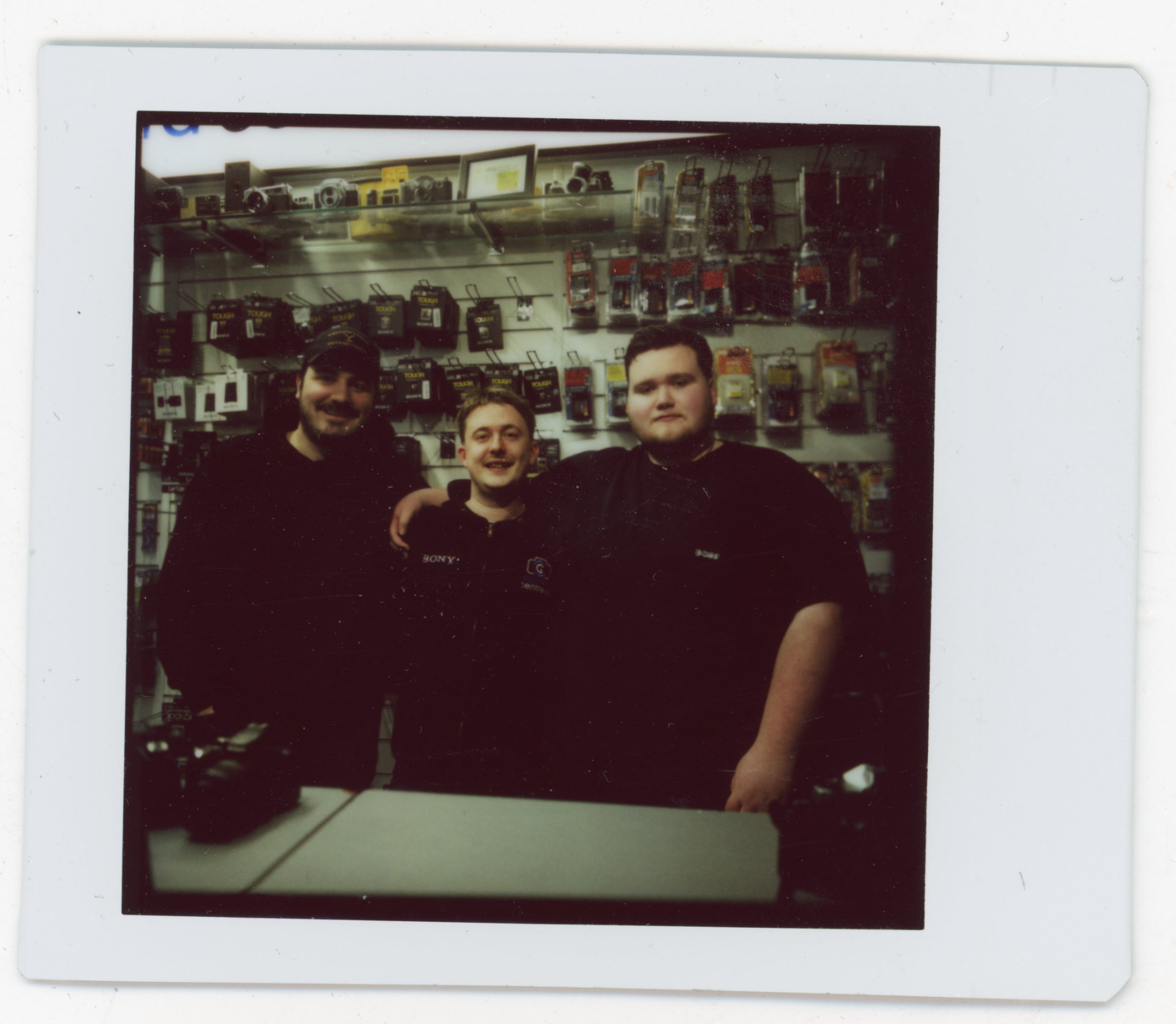 Instax photo of three Camera Centre UK staff members behind the shop counter