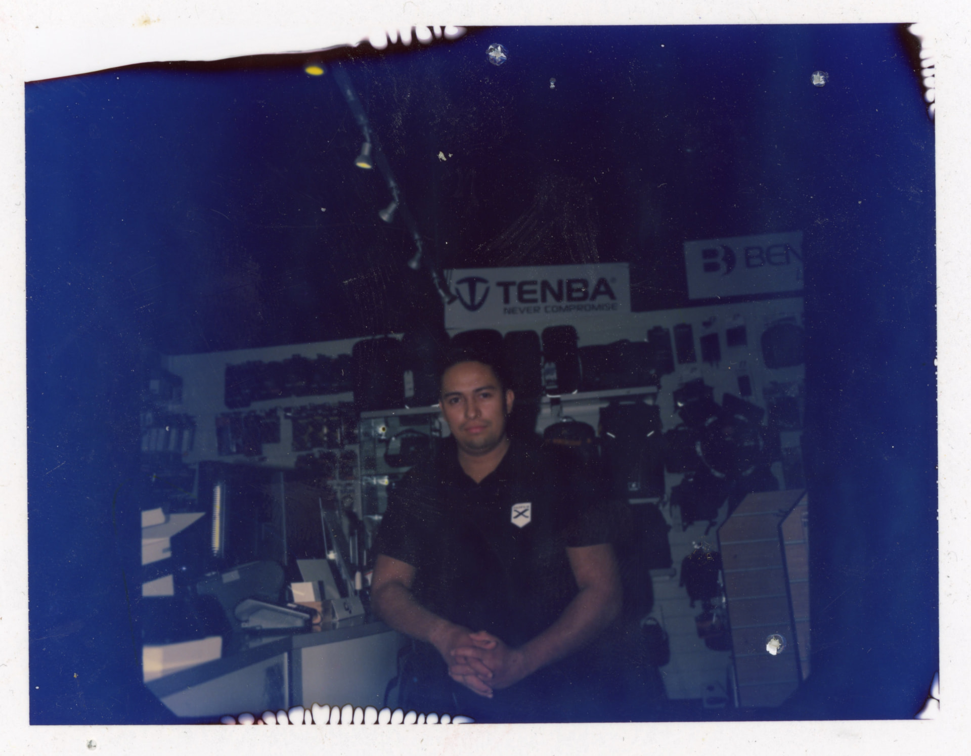 Pack film portrait of Raph sitting behind the counter at Camera Centre UK, Tenba and Benro displays behind him
