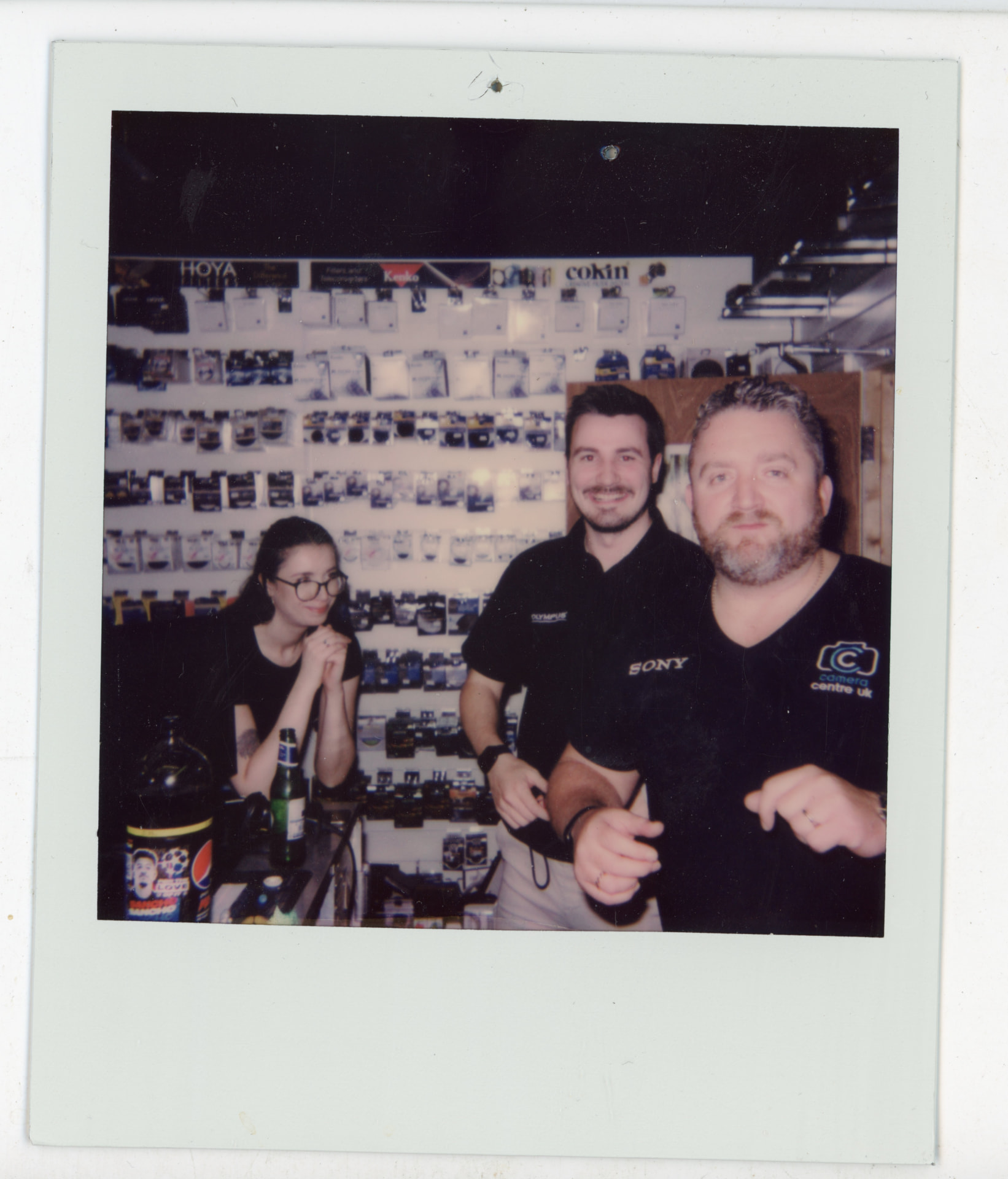 Polaroid photo of three Camera Centre UK staff members in front of the filter wall